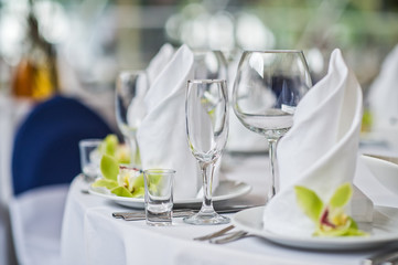 Table with glasses, plates and white napkins, green flower, dinner in the restaurant