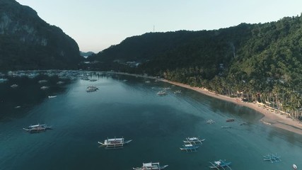 Aerial drone view of boats anchored in the bay with clear and turquoise water on the sunset. Boat and yacht in the tropical lagoon. Tropical landscape. El Nido, Palawan island, Philippines.