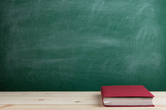 Education and reading concept - group of colorful books on the wooden table in the classroom, blackboard background