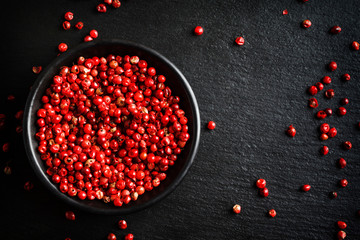 Pink peppers in bowl on black background, top view, copy space