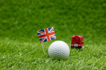 Golf ball with Union Jack flag with double decker bus on green grass