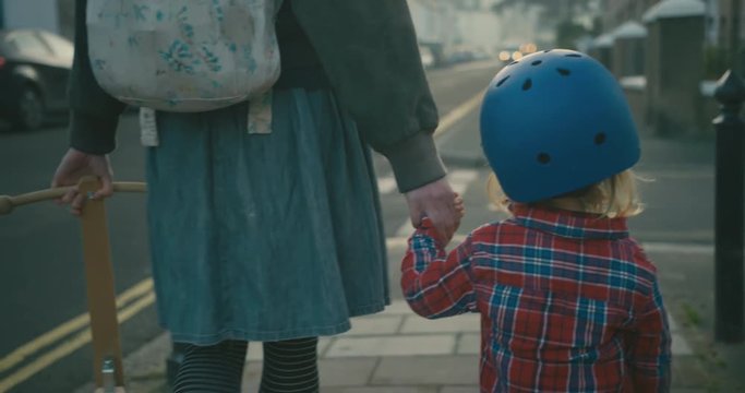Mother and little toddler with helmet holding hands as they walk down street