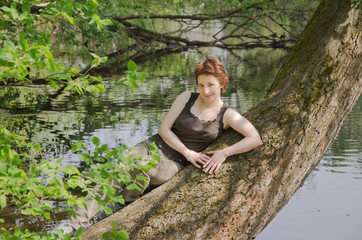 young woman resting in a forest Park in the summer on the trunk of a large tree