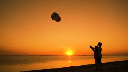 Two kids launching the rainbow kite together at sunset