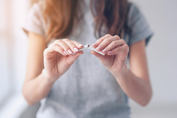 Portrait of beautiful smiling girl holding broken cigarette in hands. Happy female quitting smoking...