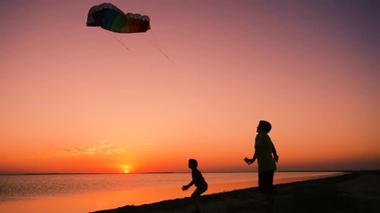 Two kids launching the rainbow kite together at sunset