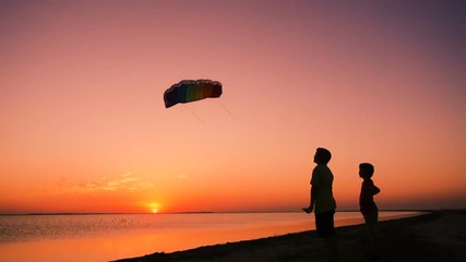 Two kids launching the rainbow kite together at sunset