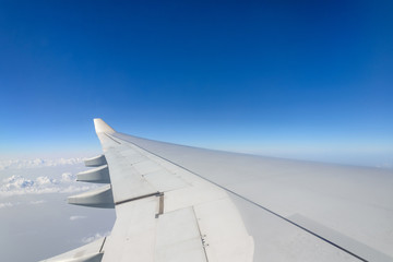 Fototapeta premium Beautiful clear deep blue sky over thick layer of clouds at stratosphere atmosphere viewed from airplane's window located above airplane's wing and jet.