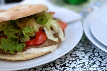 Burger in a flatbread bun with meat, lettuce, tomatoes and mayonnaise. Selective focus.