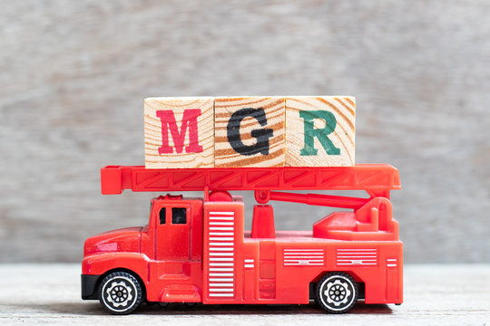 Red fire truck hold letter block in word mgr (abbreviation of manager) on wood background