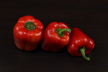 Close up.Composition. Rhythm.Three juicy red pepper are on the table with a dark background.