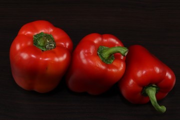 Close up.Composition. Rhythm.Three juicy red pepper are on the table with a dark background.