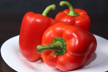 Three large red peppers lie on a white serving plate, standing on a table with a dark background.
