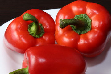 Three large red peppers lie on a white serving plate, standing on a table with a dark background.