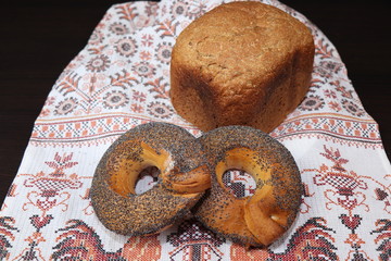 Close-up image. Still life with homemade cakes of multi-grain bread and bagels sprinkled with poppy seeds lying on a towel with hand-embroidered cocks and national patterns.