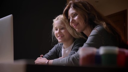 Closeup shoot of young caucasian mother with a small beautiful daughter watching a cartoon together and hugging with background isolated on black