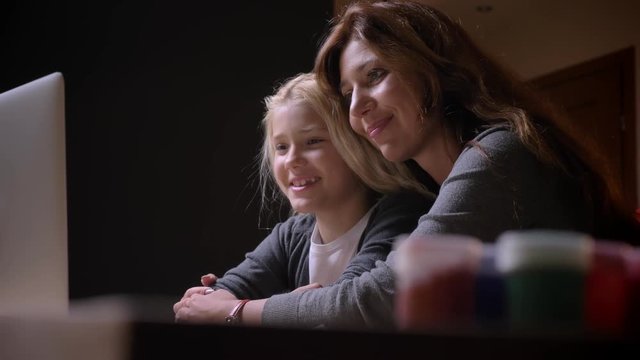 Closeup shoot of young caucasian mother with a small beautiful daughter watching a cartoon together and hugging with background isolated on black