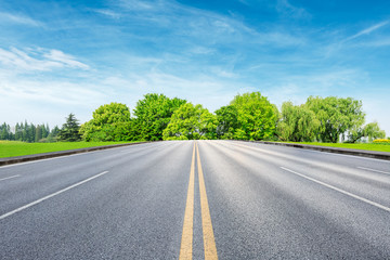 Fototapeta premium Straight asphalt road and green forest under blue sky