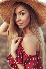 A girl in a straw hat and a red dress, in the summer in a wheat field in the village. Close-up long hair, emotions of tenderness smile and sensual look. Woman Casual makeup and tanned skin.