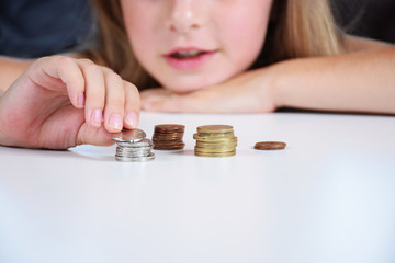 Young smiling girl counts coins on a white table