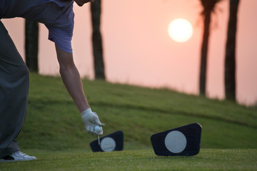 Obraz premium Golfers are putting golf ball on the teeing ground at the starting point. There is a sunrise on the background.