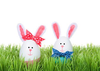 Easter Eggs crafted into bunnies, boy and girl, wearing bow tie and bow on ear sitting in green grass isolated on white background