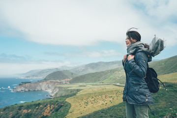 vintage photo side view of young girl backpacker with scarf flying in wind standing on mountain cliff. travel hiker trip in pacific coast highway 1 at southern end of Big Sur California usa in spring © PR Image Factory