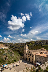Fototapeta na wymiar MATERA, ITALY - AUGUST 27, 2018: High angle summer day panoramic view over Church of Saint Peter or Chiesa di San Pietro Caveoso with white puffy clouds moving on the Italian blue sky