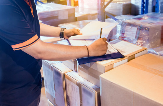 Warehouse worker writing on clipboard his checking details shipments package boxes. Commerce supply chain. Cargo shipping. Warehouse inventory managemant.