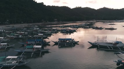 Aerial drone view of boats anchored in the bay with clear and turquoise water on the sunset. Boat and yacht in the tropical lagoon. Tropical landscape. El Nido, Palawan island, Philippines.