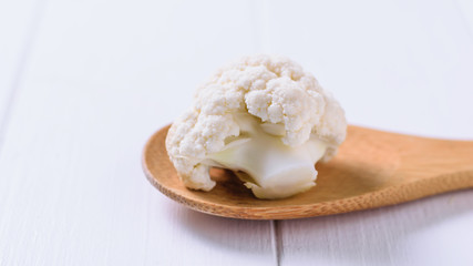Large inflorescence of cauliflower in a wooden spoon on a white table.