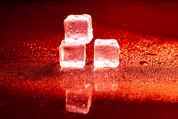 Red ice cubes reflection on black table.