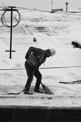 Black and white man in a vest and a helmet cleans the roof of a house from snow