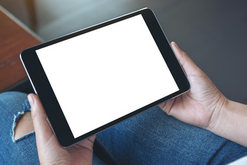Mockup image of a woman sitting and holding black tablet pc with blank white desktop screen horizontally