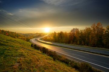Sunset over empty asphalt highway winding through autumn landscape