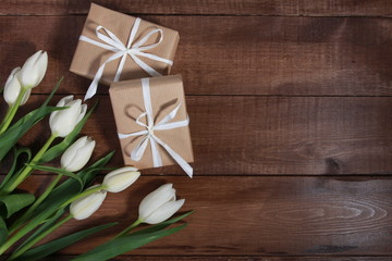 Fototapeta na wymiar White tulips and gift boxes on brown wooden table. Women day concept. White ribbon, craft wrap, 8 march, spring