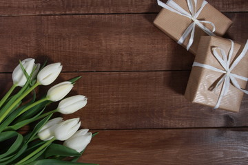 White tulips and gift boxes on brown wooden table. Women day concept. White ribbon, craft wrap, 8 march, spring