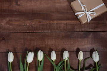 Row of white tulips and gift boxes on brown wooden table. Women day concept. White ribbon, craft wrap, 8 march, spring