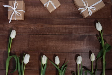 Row of white tulips and gift boxes on brown wooden table. Women day concept. White ribbon, craft wrap, 8 march, spring