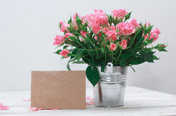 Bunch of roses in tin bucket, petals and paper badge for message on white wooden table. Women day concept. Spring, 8 march, wish, copy space, craft