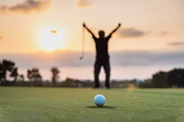 Schilderijen op glas Silhouette golfer showing happiness when win in game , white golf ball on green grass of golf course with blur background. © APchanel