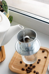 Drip, Brewing, pouring water over ground coffee contained in Vietnamese Phin Filter on windowsiil. Selective Focus.