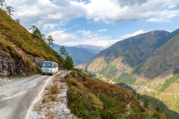 Tourist bus on mountain road with distant Himalaya snow peaks and scenic mountain valley near...
