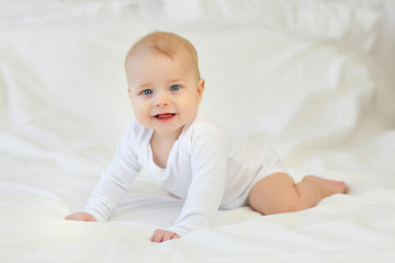 Charming blue-eyed 9 month old baby in white clothes on the bed