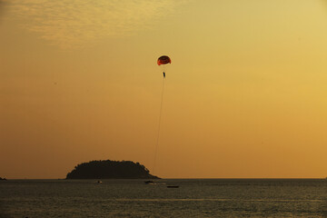 Silhouette of skydiver flies on background of sunset sky and sea 