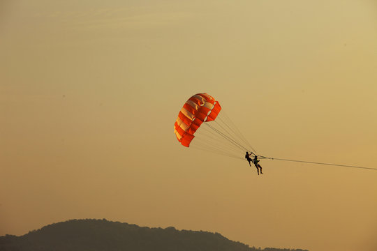 Silhouette of skydiver flies on background of sunset sky and sea 