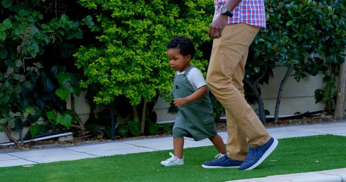 Side view of young black father and little son playing in back yard of their home 4k