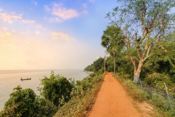 Rural village road alongside Rupnarayan river with fishing boat at sunset. Photograph taken at a village in Deulti, West Bengal India. 