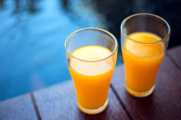 Two glasses of orange juice are placed on the wooden floor near the pool.