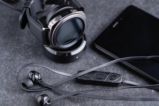 Bluetooth technology headphones, smart watches and a smartphone on a granite gray background